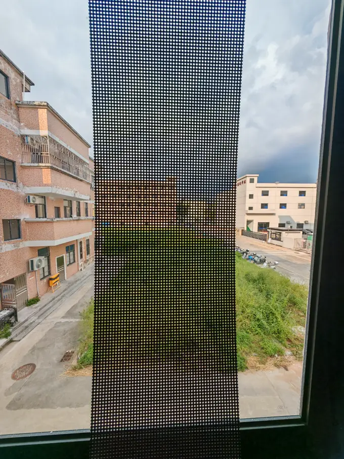 Transparent LED-film monterad på insidan av en fönsterruta, med gatan och husen utanför synliga genom bilden